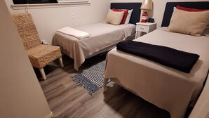 Ein Zimmer mit zwei Betten, einem Sessel, einem Nachttisch mit Lampe, einer Wanduhr und einem Willkommensschild.