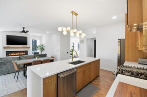 A modern kitchen with a central island, stainless steel appliances, and a dining area with a fireplace. - Sleeps 10 • New Modern Home by Swamp Rabbit Trail (Greenville)