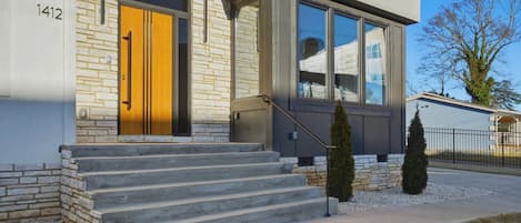 A modern building with a stone facade, a wooden door, and a staircase leading to the entrance.