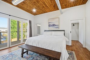 A bedroom with a large bed, a bench, a painting, and a view through the glass door. - Sleeps 10 • New Modern Home by Swamp Rabbit Trail (Greenville)
