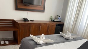 A hotel room with two beds, a wooden desk, a TV, and a minibar. - inner pease hotel (Anuradhapura)