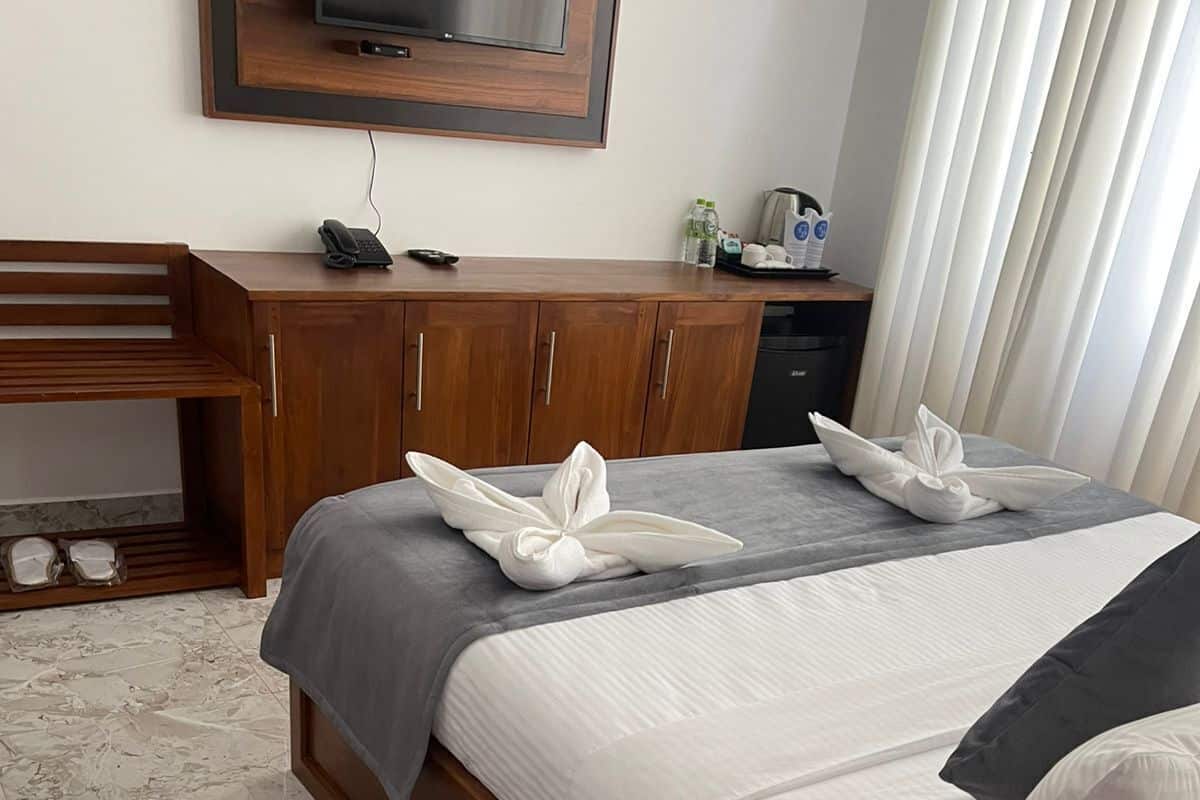 A hotel room with two beds, a wooden desk, a TV, and a minibar.
