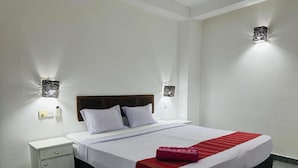 A neatly made bed with a red blanket, a wooden headboard, and two bedside lamps. - inner pease hotel (Anuradhapura)
