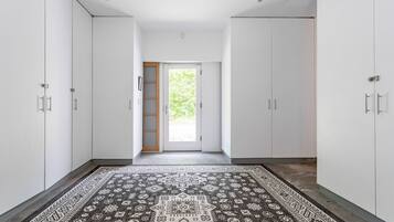 Un couloir avec des armoires blanches, un tapis à motifs et une porte donnant sur l’extérieur.
