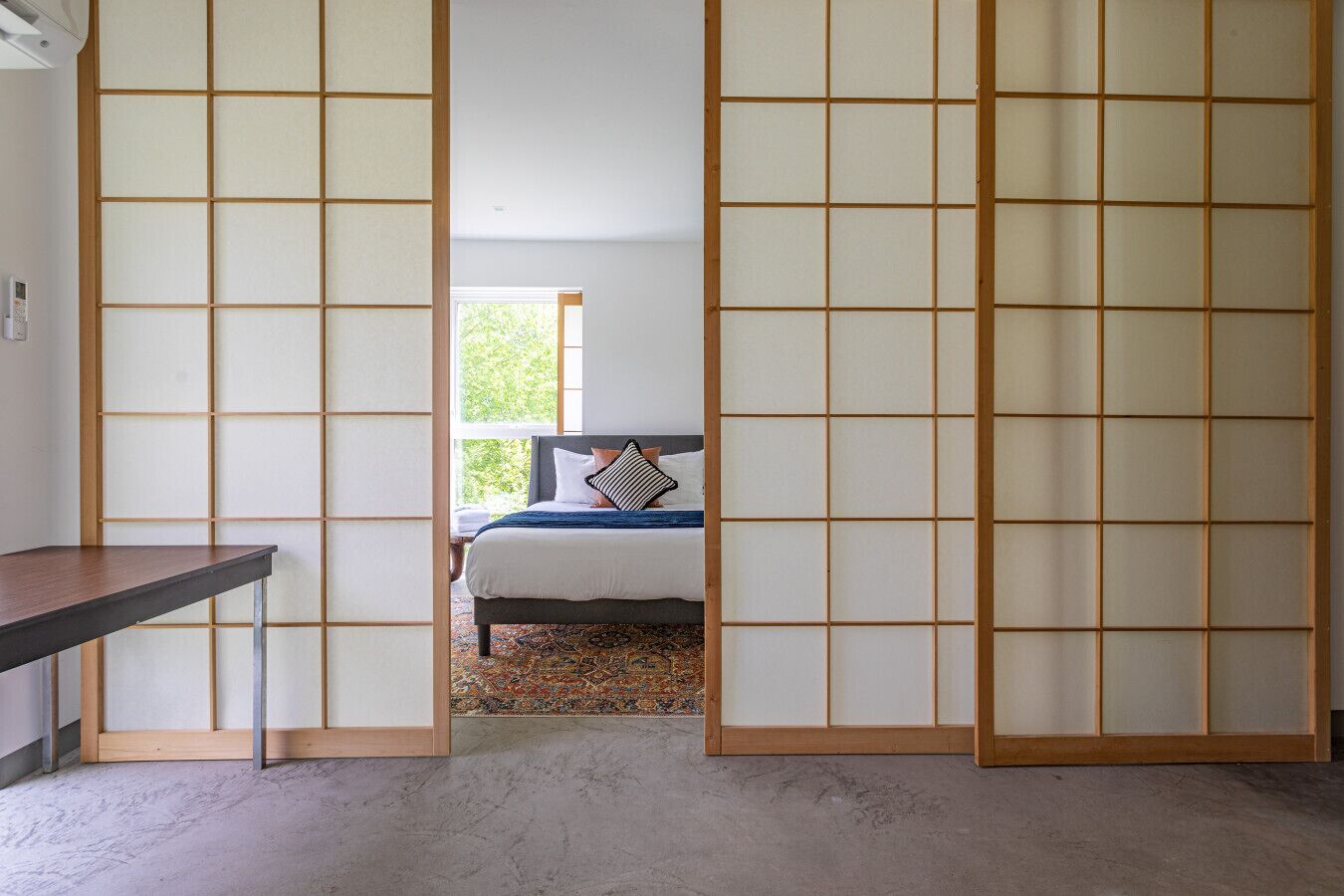 Quarto com cama, escrivaninha e vista para o exterior pela janela.