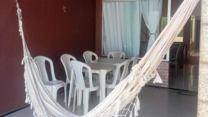 Ein Zimmer mit einer weißen Hängematte, weißen Plastikstühlen, einem Tisch und einer roten Pendelleuchte.