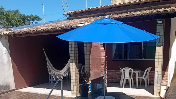 Ein Schwimmbecken mit blauem Sonnenschirm, einer Hängematte und einer Terrassenanlage mit Stühlen und Tisch.