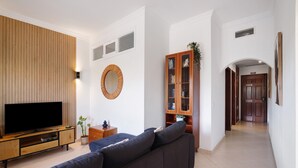 Un salon doté d’un téléviseur à écran plat, d’un canapé foncé, d’un mur recouvert de panneaux de bois et d’un meuble avec des portes en verre.