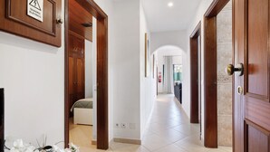 Un couloir avec des portes en bois, un sol carrelé et un panneau indiquant un danger électrique.