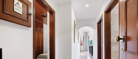 A hallway with wooden doors, a tiled floor, and a sign indicating an electrical hazard.