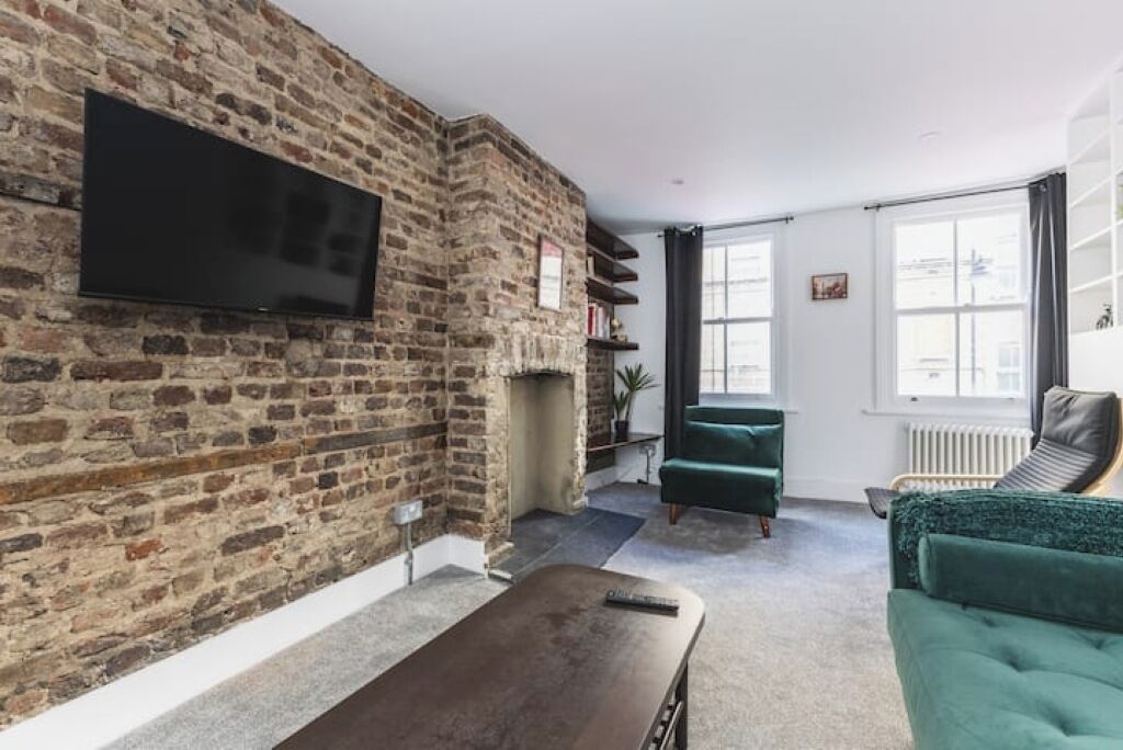 Un salon avec un mur en pierre, un téléviseur à écran plat, une cheminée, un fauteuil vert et un canapé.