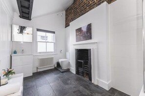 A bathroom with a white sink, toilet, and a fireplace. - The Victorian Maisonette – Timeless Elegance in the Heart of London (London)