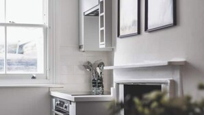 Een keuken met witte kastjes, een raam en een open haard.