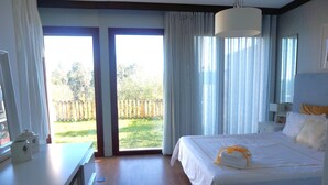 Ett hotellrum med en stor säng, ett skrivbord och utsikt över en gräsklädd innergård genom en skjutdörr av glas.