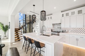 A modern kitchen with a large island, white cabinetry, and a staircase leading to an upper level. - Rooftop Hot Tub | Gulf Views | Walk to Beach (Inlet Beach)