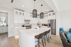 A modern kitchen with white cabinetry, a central island with bar stools, stainless steel appliances, and pendant lighting. - Gulf View Home with Rooftop Hot Tub, Bikes and Elevator (Inlet Beach)