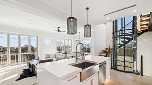 Een moderne keuken met een groot eiland, roestvrijstalen apparatuur en hanglampen.