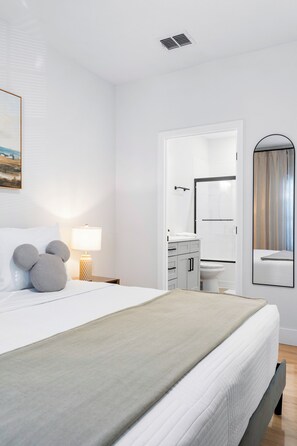 A modern hotel room with a neatly made bed, a bedside lamp, a large mirror, and a bathroom visible through an open door. - Elegant Modern Townhome with Themed Bedrooms Close to Clubhouse (Kissimmee)