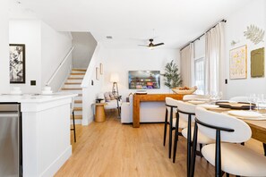 A modern kitchen with a wooden island, white cabinetry, and a dining area with a wooden table and white chairs. - Elegant Modern Townhome with Themed Bedrooms Close to Clubhouse (Kissimmee)
