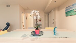 Una habitación con una mesa de comedor, sillas, una orquídea en maceta, un cuadro y una puerta que da a otra habitación.