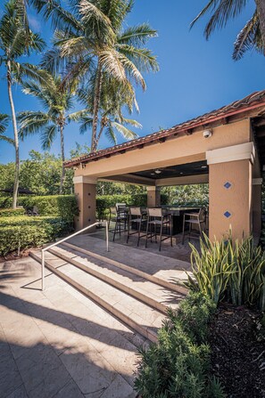 An outdoor patio with a covered seating area, palm trees, and a well-maintained garden. - Stylish 2BR/2BA Getaway - Pool, Tennis Court & Free Parking (Aventura)