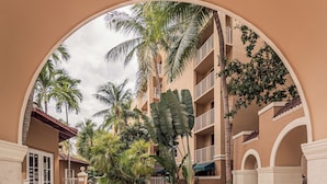 Un patio con una fuente central, rodeado de palmeras y un edificio de varios pisos con balcones.