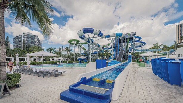 Un parque acuático con múltiples toboganes y piscinas, rodeado de palmeras y sillas de descanso.