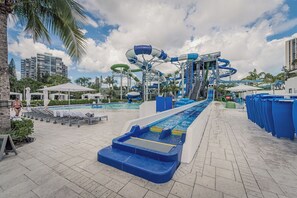 A water park with multiple slides and pools, surrounded by palm trees and lounge chairs. - Stylish 2BR/2BA Getaway - Pool, Tennis Court & Free Parking (Aventura)