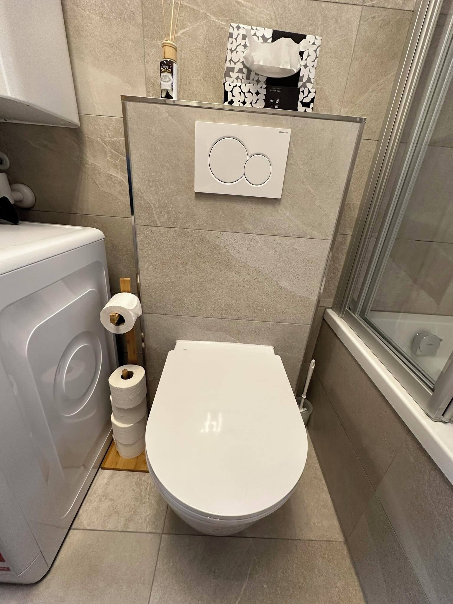 Une salle de bain moderne équipée de toilettes, d’un lave-linge et d’un espace douche.