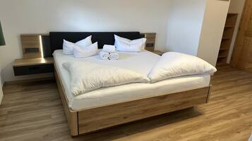 Una cama bien hecha con sábanas y almohadas blancas, cabecera de madera y una mesita de noche con lámpara.