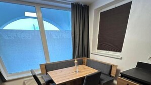 A compact room with a wooden table and chairs, a small kitchenette, and a large window offering a view. - Apart Bader (Ehrwald)