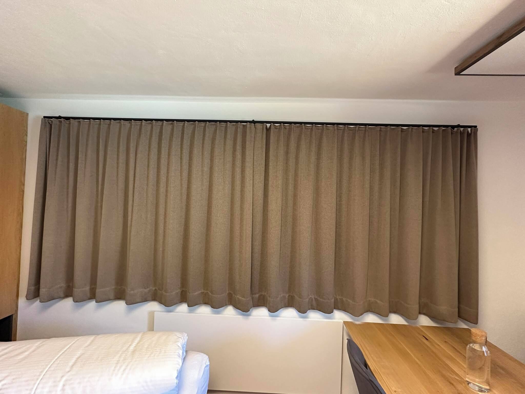 A bedroom with a bed, a wooden nightstand, and a window with brown curtains.