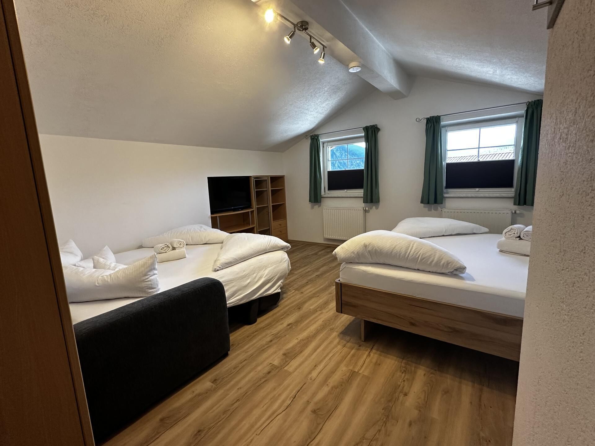 Una habitación con dos camas, televisión, piso de madera y ventana con cortinas.
