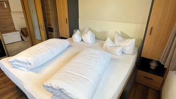A double bed with white linens and pillows, a wooden headboard, and a wooden floor.