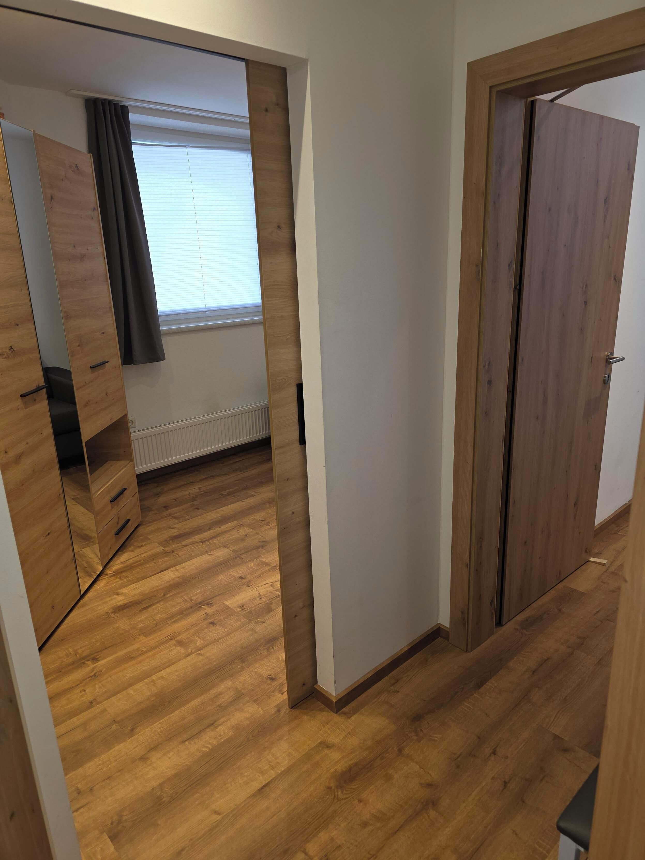 Quarto com piso de madeira, janela com persianas, porta e guarda-roupa.
