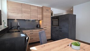 A modern kitchen with wooden cabinets, a built-in oven, and a dining table with a potted plant. - Apart Bader (Ehrwald)
