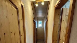 A narrow hallway with wooden doors and a tiled floor, leading to a small window at the end. - Apart Bader (Ehrwald)
