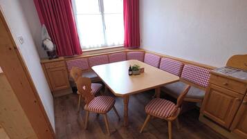 A dining area with a wooden table and checkered chairs, a window with red curtains, and a gnome decoration.