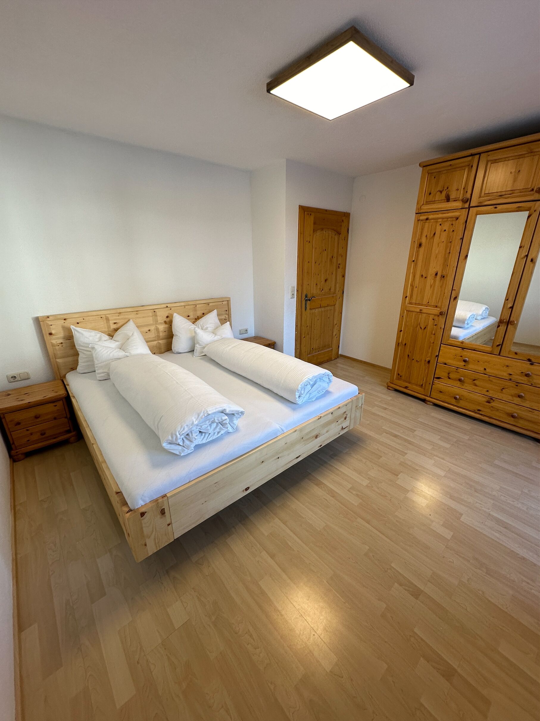 Un dormitorio con una cama de madera, una mesita de noche, un armario y un espejo.