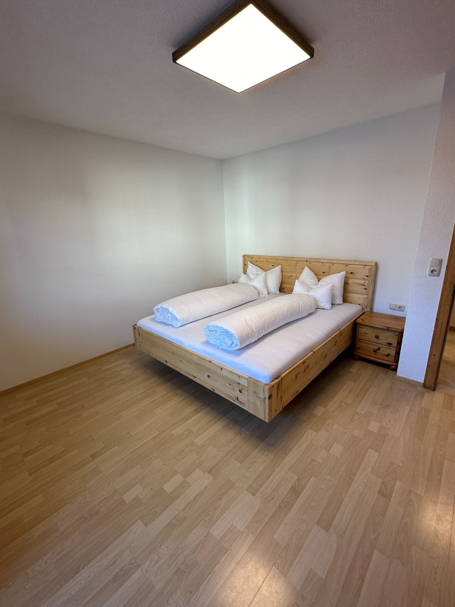 A bedroom with a wooden bed, white bedding, and a nightstand.