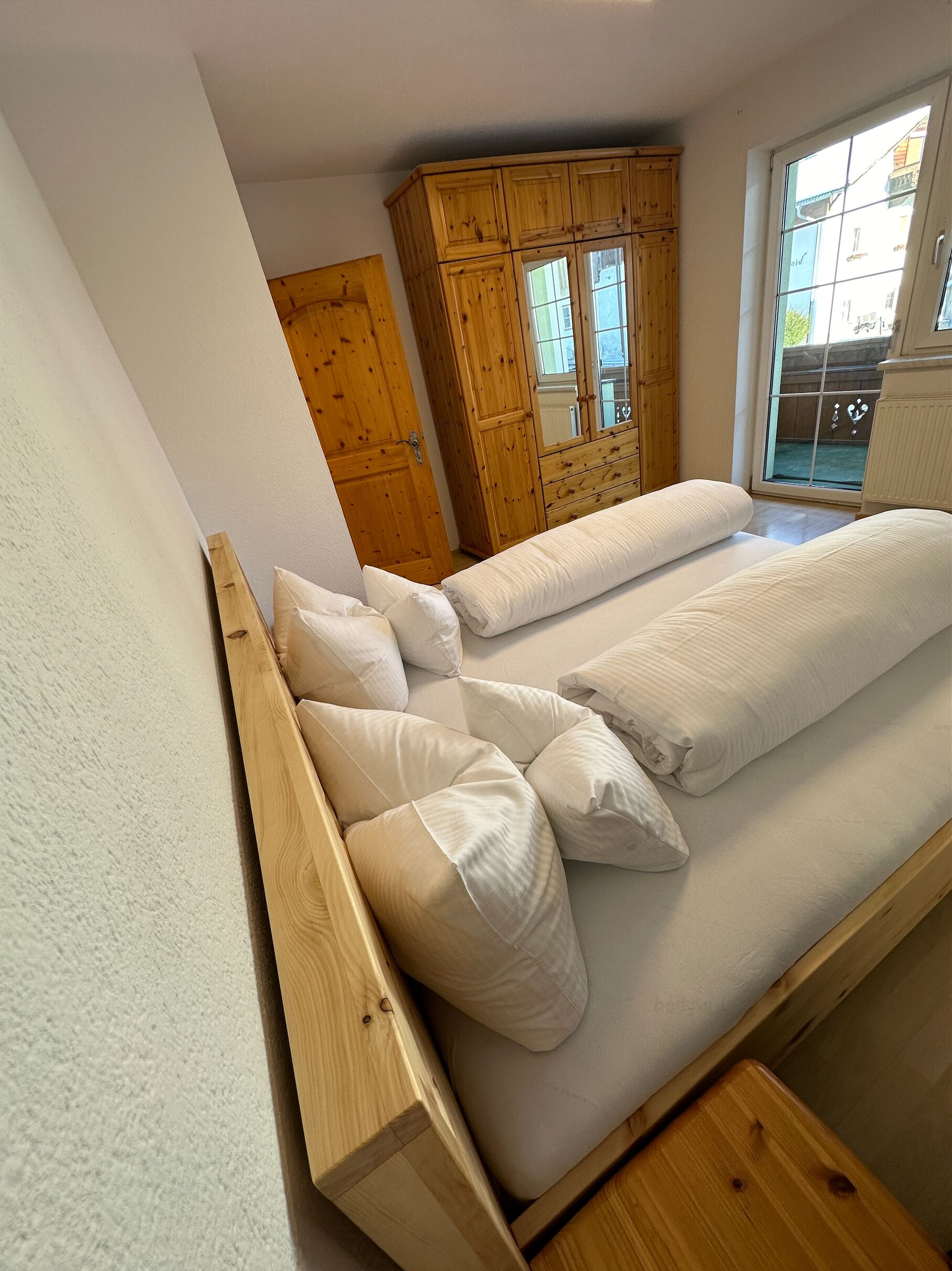 A bedroom with a wooden bed frame, white bedding, and a wooden wardrobe.