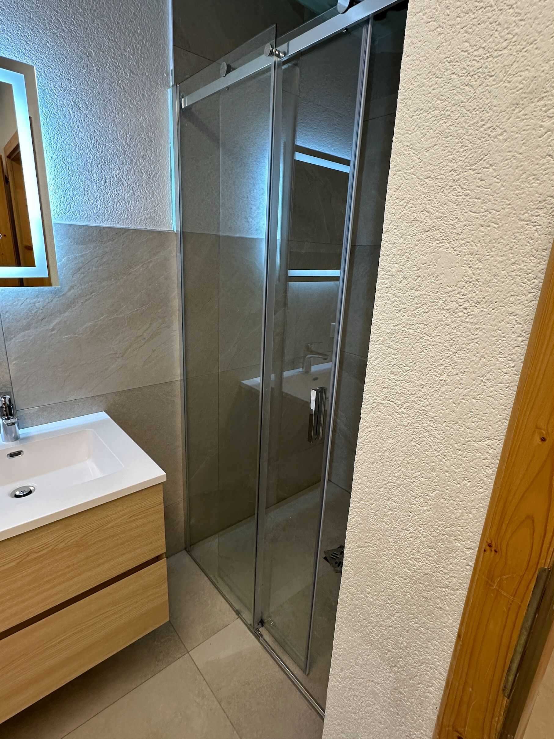 A bathroom with a glass-enclosed shower, a wooden vanity with a sink, and a mirror.