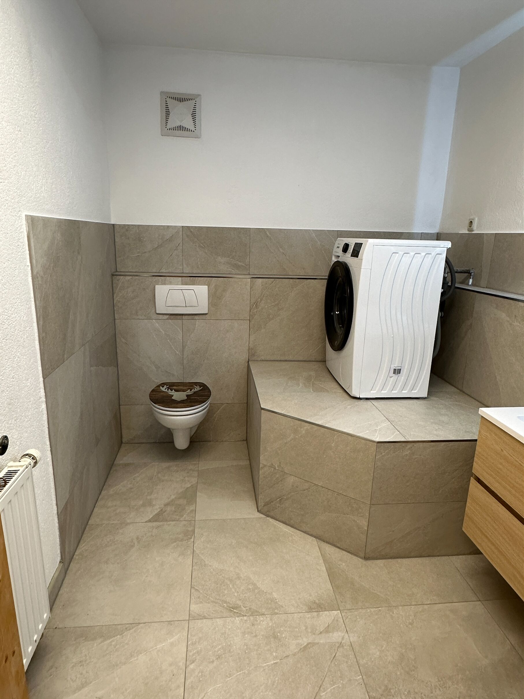 A compact bathroom with a toilet, a washing machine, and a radiator.