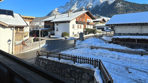 A snowy village with traditional wooden houses, a stone wall, and a mountain in the background. - Apart Bader (Ehrwald)