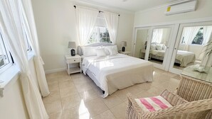 Une chambre à coucher avec un grand lit, deux tables de chevet avec des lampes, un miroir et un fauteuil en osier.