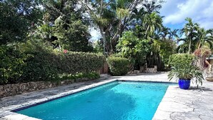 Une piscine rectangulaire dont le bord est recouvert de carreaux, entourée d’une terrasse en pierre et d’une végétation luxuriante.