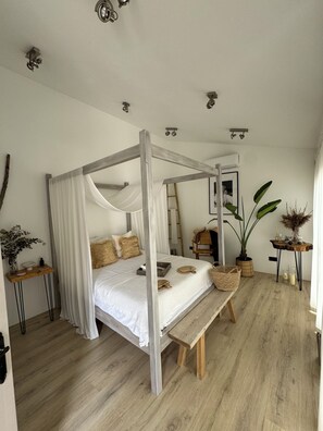 Ein Bett mit Baldachin, ein Nachttisch mit Lampe, eine Bank und ein Blumentopf.
