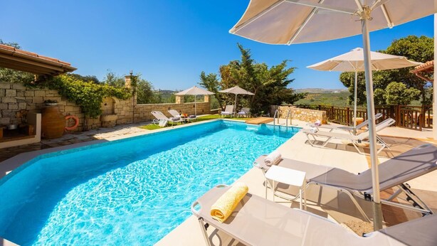 Ein Pool mit Liegestühlen und Sonnenschirmen, umgeben von Steinmauern und viel Grün.