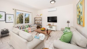 Ein Wohnzimmer mit einer Couch, einem Couchtisch mit Obst, einem Fernseher und einem Bücherregal.