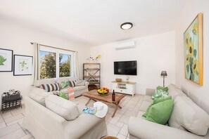 A living room with a sofa, a coffee table with fruit, a TV, and a bookshelf. - Villa Korini - Four Bedroom Villa, Sleeps 8 (Achlades)